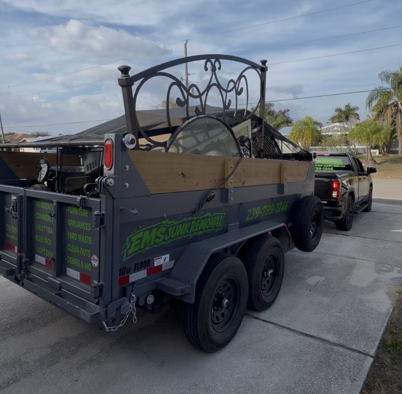 EMS Junk Removal trailer loaded with a bed frame and cleanout junk, hitched to the truck in a Southwest Florida driveway