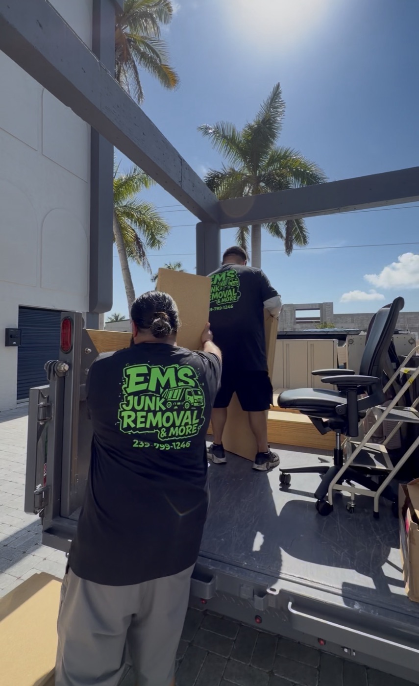 EMS Junk Removal crew in branded shirts loading office furniture onto the truck liftgate